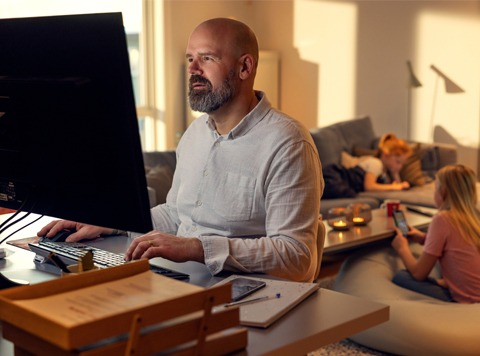 Mann ser på PC med ny hjemmesentral i stuen med barna i bakgrunnen