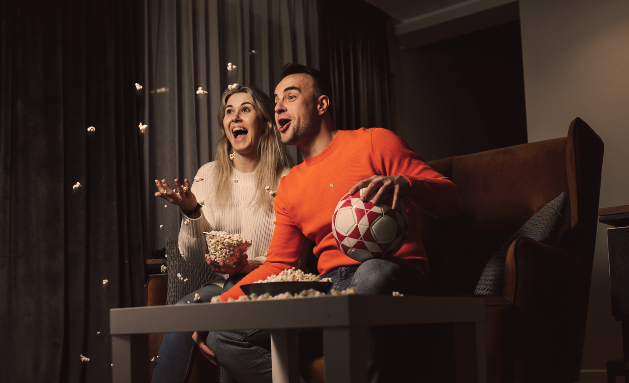 young cheerful family cheering on comfortable brown sofa. Looking at TV and having fun of match. Close-up photo Par ser på fotball.