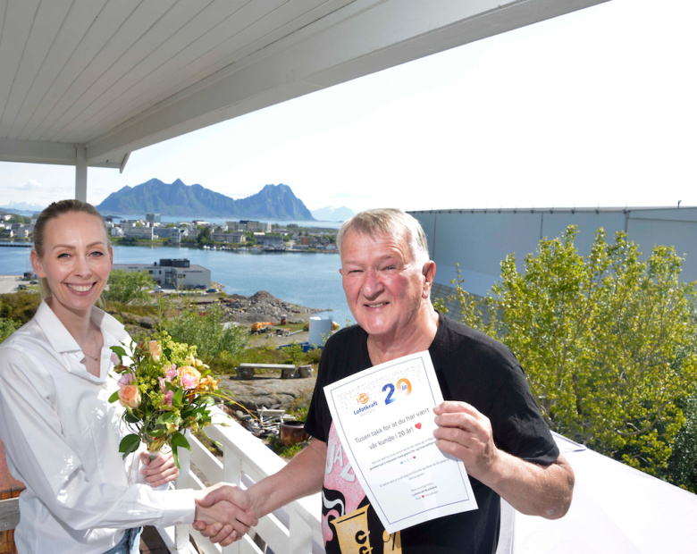 20-ÅRSJUBILEUM: Forfatter og journalist John-Arne Storhaug (75) har vært kunde siden 2005. Ida Malnes, salgs- og markedskonsulent i Lofotkraft Bredbånd, takker med blomster.  Foto: Tore Berntsen Visualdays.no
